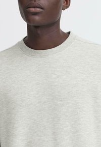 Light grey crewneck sweatshirt with a soft, textured fabric. Features ribbed collar and a simple, minimalistic design.
