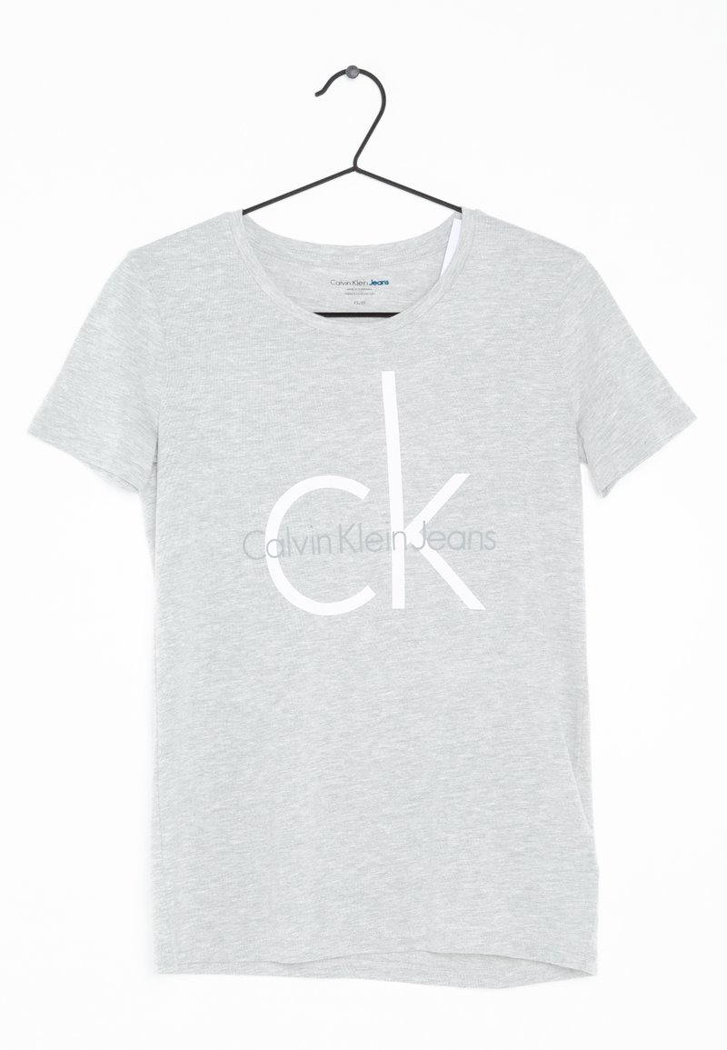 Camiseta de manga corta gris hecha de tejido suave, con un gran logo blanco "CK" y el texto "Calvin Klein Jeans" impreso en el centro.