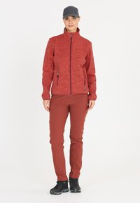 Röd fleecejacka med dragkedja fram och sidofickor, tillsammans med smala, mörkröda byxor och svarta vandringskängor.