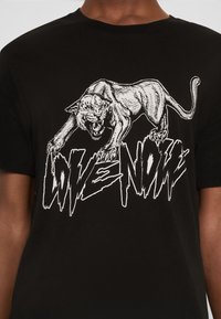 Czarna koszula z białą grafiką wściekłego pantery nad wyrazistym, postrzępionym napisem "LOVE NONE" na wysokości klatki piersiowej.