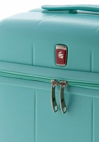 Maleta rígida de color turquesa con tiradores de doble cremallera y una pequeña placa de logo de Gladiador roja en el panel frontal.