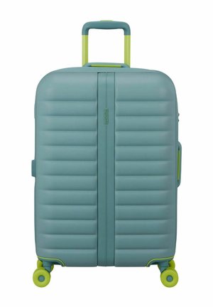 Valise rigide bleue avec des rainures horizontales, poignée télescopique jaune-vert et quatre roulettes pivotantes jaune-vert, vue de face en position verticale.