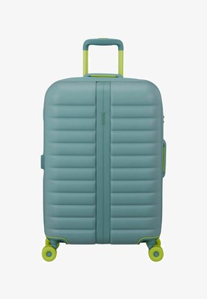 Valise rigide bleue avec des rainures horizontales, poignée télescopique jaune-vert et quatre roulettes pivotantes jaune-vert, vue de face en position verticale.