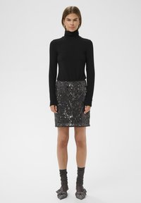 Fekete garbós felső, ami egy illeszkedő fekete flitteres szoknyával van párosítva. A szoknya fényvisszaverő flitterekkel és sima felülettel rendelkezik. Szürke bokazokni és kötött cipők.