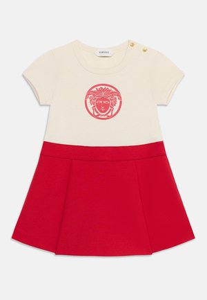 Rochie pentru copii mici cu mâneci scurte, crem și roșu, cu logo Medusa pe piept, nasturi aurii pe umăr și fustă roșie plisată.