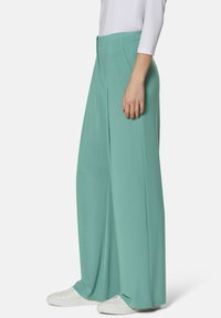 Mint green wide-leg trousers with a smooth texture, featuring a tailored waistband and side pockets, paired with white sneakers.