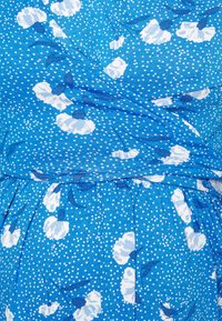 Tecido azul com padrão floral branco e pequenas bolinhas brancas. Superfície texturizada com um design drapeado, apresentando pregas franzidas na cintura.