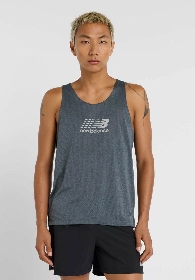 Jongere met kort blond haar, gekleed in een grijze New Balance tanktop en zwarte shorts, staand tegen een effen lichte achtergrond.
