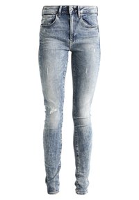 Jeans de corte ajustado en denim azul claro, con un lavado deslavado, acentos desgastados, cinco bolsillos y un cierre clásico de botón y cremallera.