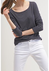 Granatowo-biały top z długim rękawem w paski o dekolcie w łódkę, zestawiony z białymi spodniami. Tkanina wydaje się miękka, a sylwetka dopasowana.