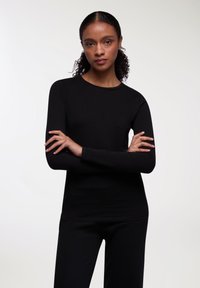 Top lungo nero a maniche con collo a giro e silhouette aderente, realizzato in tessuto morbido e elastico. Texture liscia, senza motivi visibili.