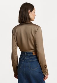 Bronzas satīna blūze ar šalu apkakli un garām piedurknēm, kombinēta ar tumšo džinsu svārku, kuram ir aizmugurējās kabatas un ādas birka.