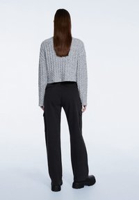 Pull gris texturé et court associé à un pantalon cargo noir taille haute. Chaussures à semelles épaisses, vue de dos.