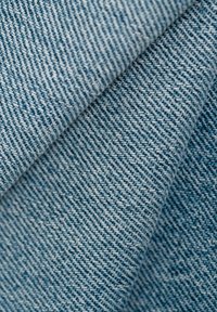 Denimstoff in hellblauen Nuancen, mit klassischem Köpergewebe, sichtbaren Nahtmustern und glatter Textur.