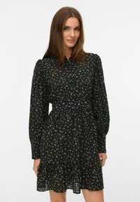Zwarte jurk met een bloemenpatroon in groen en wit, lange poffcuffs, een knoopsluiting aan de voorkant en een uitlopende zoom.