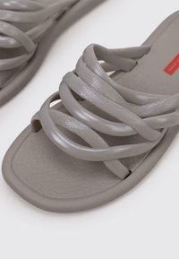 Chanclas de plástico grises con tiras entrecruzadas y suelas texturizadas. Presenta un acabado suave y un diseño minimalista.