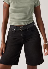 Άτομο που φοράει μαύρα τζιν σορτς μέχρι το γόνατο με μαύρη ζώνη και κοντό τοπ με πράσινες και λευκές ρίγες.