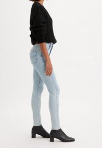 Suéter de punto negro, jeans ajustados de mezclilla azul claro y botines negros con tacón bloque. La vista lateral destaca la textura y el ajuste.