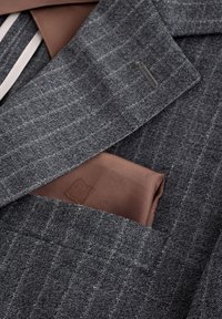 Veste de costume gris à fines rayures avec un mouchoir de poche marron soigneusement rangé dans la poche poitrine.