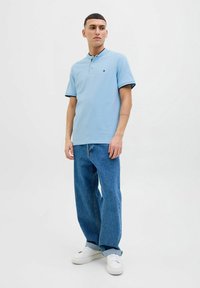 Polo shirt azzurro con maniche corte, design a tinta unita, due bottoni sul colletto, abbinato a jeans blu larghi e sneakers bianche.