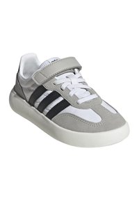 Sneaker bianco e grigio con strisce nere, lacci bianchi e un cinturino in velcro grigio su uno sfondo bianco.