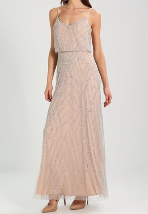 Woman wearing a floor-length, nude-pink sequin gown with spaghetti straps and nude pointed heels against a plain background.