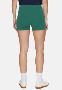 Gröna shorts med hög midja, tillverkade av elastiskt material. Baksidan visar en jämn yta och minimala sömmar. Vita sneakers och strumpor är synliga.