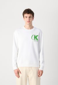 Fehér, klasszikus nyakú pulóver, pamutból készült, bal mellen nagy zöld "CK" logóval és "Calvin Klein" felirattal. Egyszerű dizájn, bordás mandzsetták.