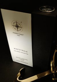 Huisgeur doos met een glanzend witte voorkant met een kompasontwerp en tekst. Bevat gouden accenten en een gebogen metalen haak.