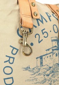 Leinentasche in hellbeiger Farbe mit blauem Druckdesign und einem Lederband mit Messingbeschlägen und Federhakenverschluss.