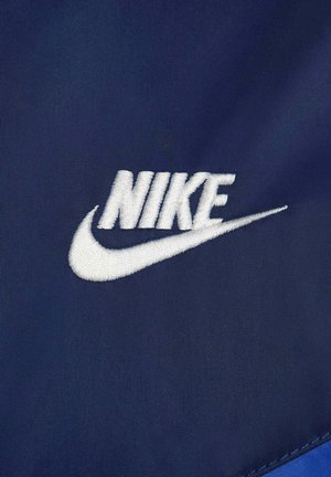 Dunkelblauer Stoff mit einem weißen gestickten Nike-Logo und einem Swoosh-Design, das eine glatte Textur und klare Linien präsentiert.