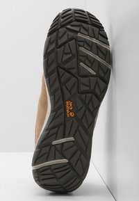 Brown suede boot sole with black rubber traction pattern. Features deep treads and a yellow "Jack Wolfskin" logo. Durable and rugged design.