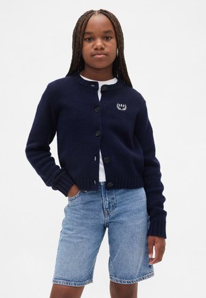 Marineblå strikcardigan med rund hals, syv knapper og ribstrikkede manchetter, med en lille broderet logo på venstre bryst.