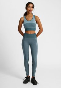 Teal sportbh met verticale strepen en bijpassende high-waisted leggings met contrasterende zijstrepen. Zwarte sportschoenen maken de outfit compleet.