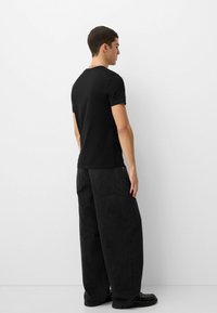 Fekete, rövid ujjú póló, laza szabású fekete farmernadrággal párosítva. Simaság jellemzi az anyag textúráját, minimális design, és klasszikus, kerek nyakú fazon.