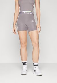 Shorts atletici gri cu dungi albe și un tiv asortat. Materialul este neted și elastic, conceput pentru îmbrăcăminte sportivă.