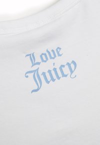 Bijela pamučna majica s okruglim izrezom s natpisom "Love Juicy" u svijetloplavom gotičkom fontu. Glatka tekstura, minimalistički dizajn.