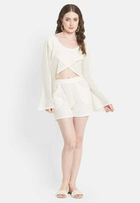 Divadādas divdaļīgā apģērba komplekts off-white krāsā. Iekļauj iezīmētu garām piedurknēm augšdaļu ar pārklājošu dizainu un šortus ar priekšējām kabatām.