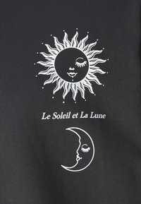 Černá tkanina s bílým grafickým ztvárněním slunce a měsíce s obličeji, pod designy doplněná textem "Le Soleil et La Lune".