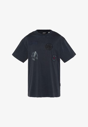 T-shirt bleu marine foncé à manches courtes avec plusieurs patches noirs, dont un emblème de crâne, un patch "US 740 N" et un badge rouge numéro 3.