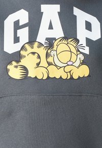 Felpa grigia con un grande logo bianco "GAP" e un'illustrazione cartoon di un gatto giallo addormentato con strisce nere.