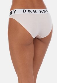 Biancheria intima di colore chiaro con un elastico bianco in vita recante la scritta nera "DKNY". Tessuto morbido, design senza cuciture, con copertura posteriore moderata.