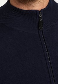 Navy zip-up sweater with a high collar and textured knit fabric. Features a black zipper and subtle ribbed accents at the collar.