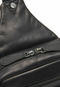 Interno di una borsa in pelle nera con una texture liscia, tasca con cerniera e cuciture visibili con un accento metallico vicino alla parte superiore.