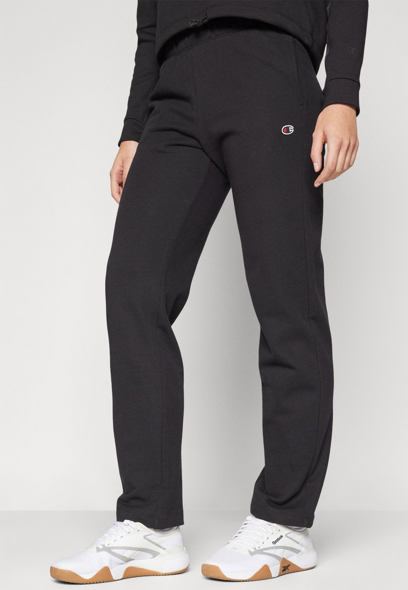 Pantaloni della tuta neri con vita elastica, gambe dritte e tasche laterali. Presenta un piccolo logo sulla coscia sinistra. Abbinati a sneakers bianche.