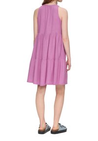Lila ärmelloses Kleid mit einem gestuften Design, leichtem Stoff und einem gerafften Ausschnitt, kombiniert mit blauen Slippern mit dicker Sohle.
