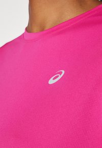 Ljusrosa t-shirt gjord av slät tyg, har en rund halsringning och en liten silverlogotyp på bröstet. Kortärmade.