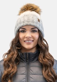 Bonnet tricoté gris avec un motif texturé, surmonté d'un grand pompon en fausse fourrure, assorti à une veste noire à zip.