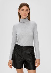 Un pull col roulé gris en tissu doux, associé à un short en cuir noir à taille haute et à la coupe structurée.