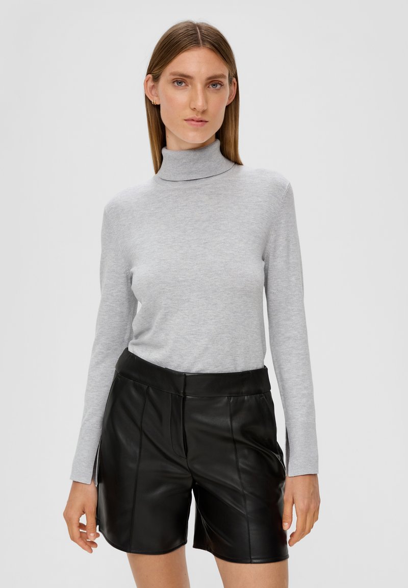 Un pull col roulé gris en tissu doux, associé à un short en cuir noir à taille haute et à la coupe structurée.